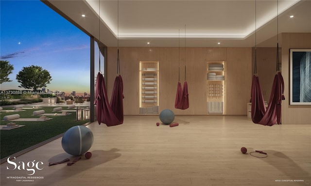 exercise area featuring a tray ceiling, wooden walls, and light wood-type flooring