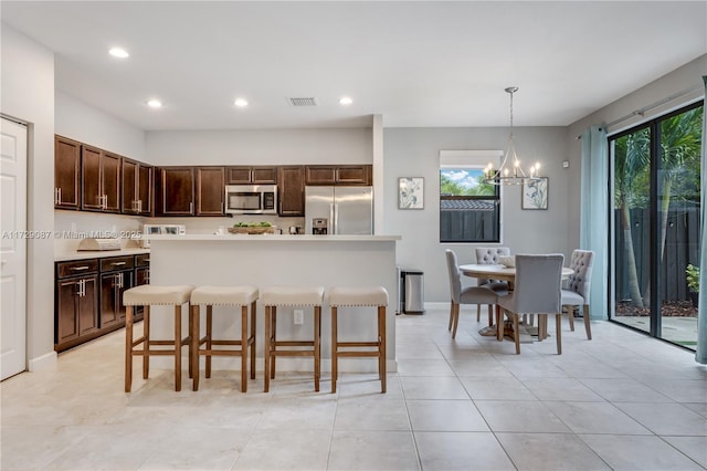 kitchen featuring a center island, decorative light fixtures, stainless steel appliances, dark brown cabinets, and a breakfast bar area