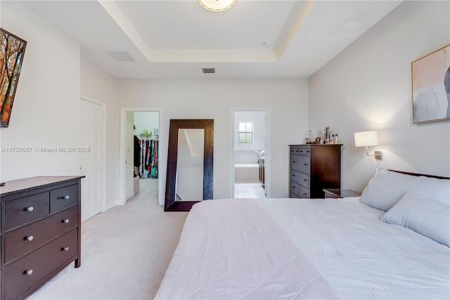 bedroom with a spacious closet, light carpet, a closet, a raised ceiling, and ensuite bathroom