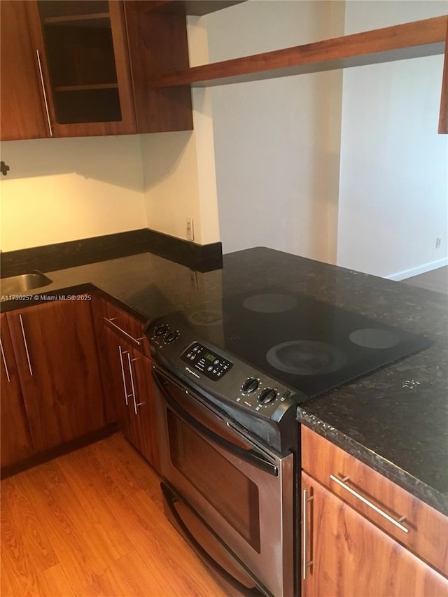 kitchen with stainless steel electric range oven, light wood-type flooring, and dark stone counters