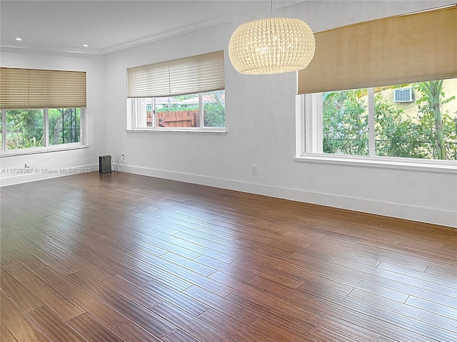 empty room with dark hardwood / wood-style flooring, ornamental molding, plenty of natural light, and an inviting chandelier