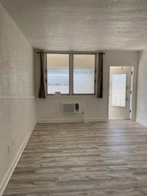 empty room featuring wood-type flooring, a wall mounted AC, and a textured ceiling