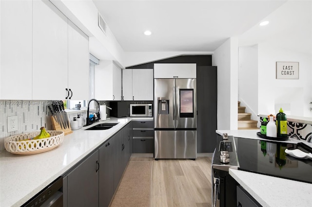 kitchen featuring appliances with stainless steel finishes, white cabinetry, decorative backsplash, sink, and light wood-type flooring