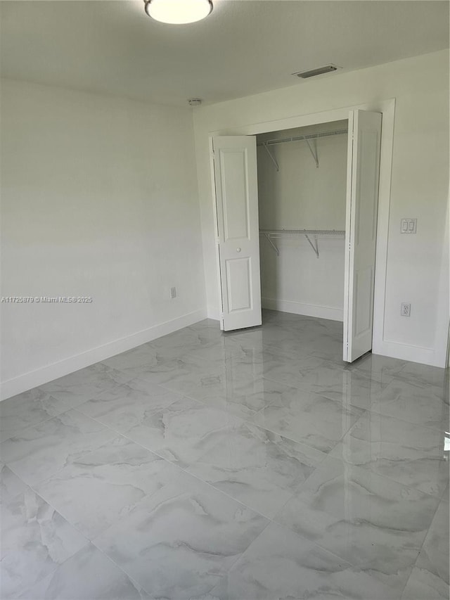 unfurnished bedroom with marble finish floor, baseboards, visible vents, and a closet