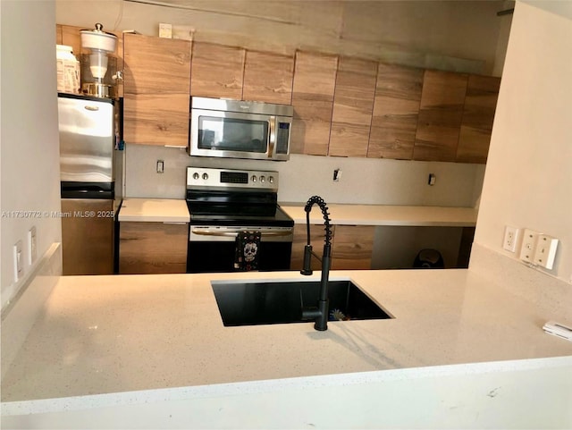 kitchen featuring light stone counters, stainless steel appliances, and sink