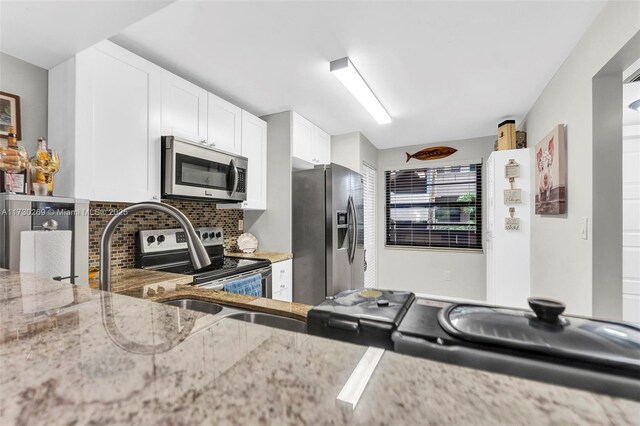 kitchen with light hardwood / wood-style floors, white cabinets, backsplash, stainless steel appliances, and light stone counters