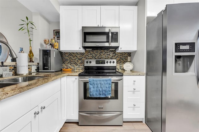 kitchen featuring light stone countertops, white cabinetry, sink, backsplash, and stainless steel appliances