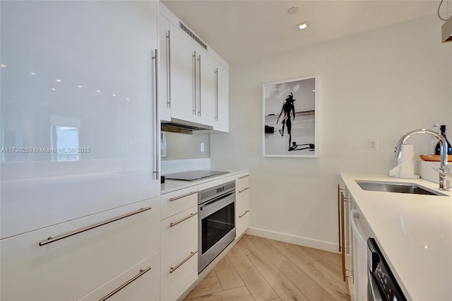 kitchen with white cabinets, sink, oven, light wood-type flooring, and black electric cooktop