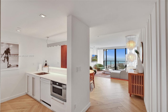 kitchen featuring white dishwasher, sink, stainless steel oven, and light parquet flooring