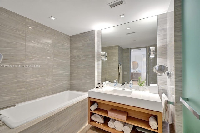 bathroom with tiled bath, tile walls, and vanity