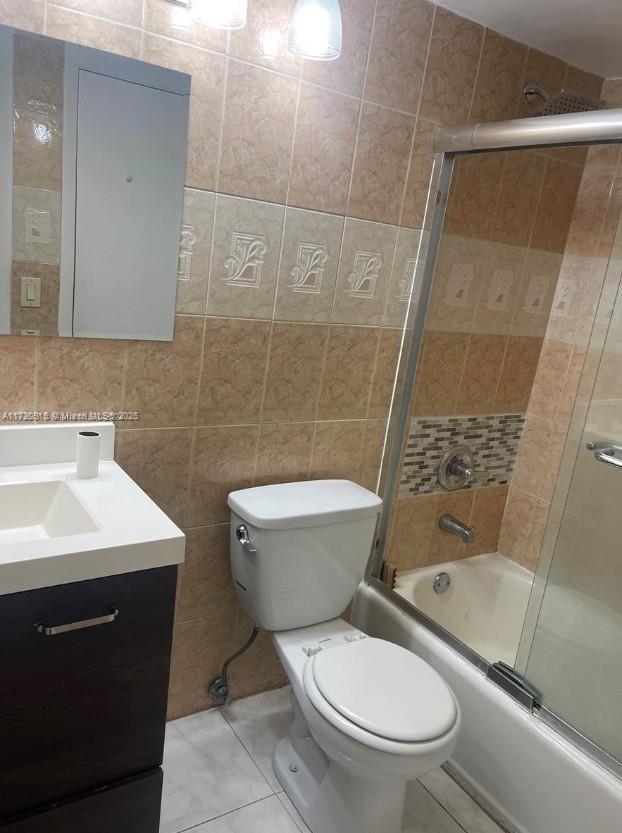 full bathroom featuring toilet, bath / shower combo with glass door, tile walls, tile patterned flooring, and vanity