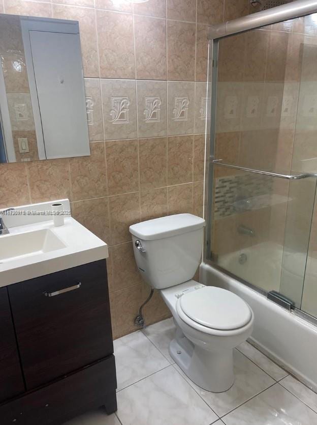 full bathroom featuring tile patterned flooring, vanity, bath / shower combo with glass door, tile walls, and toilet