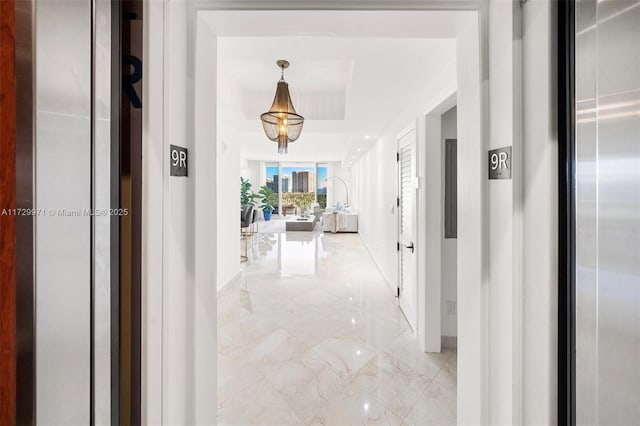 hallway featuring marble finish floor, baseboards, elevator, and a raised ceiling