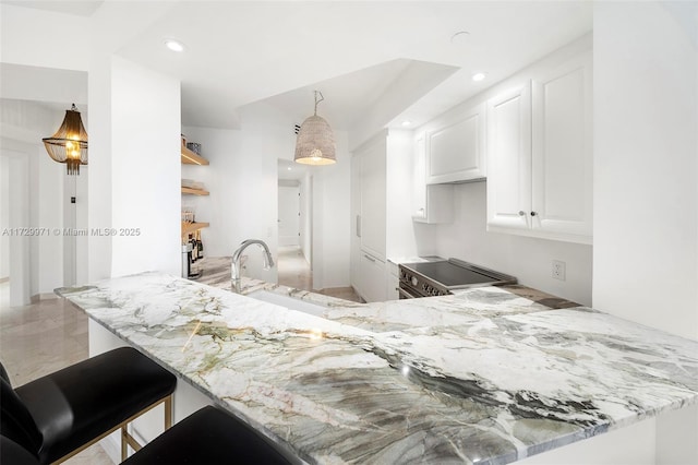 kitchen with white cabinets, light stone counters, a sink, stainless steel electric range, and a peninsula