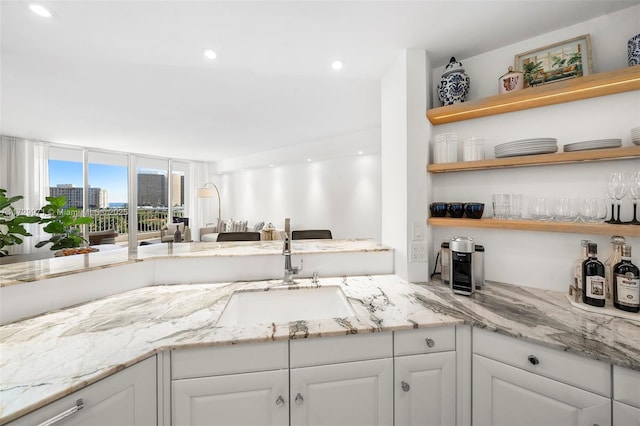 kitchen featuring open shelves, white cabinets, a sink, and light stone counters