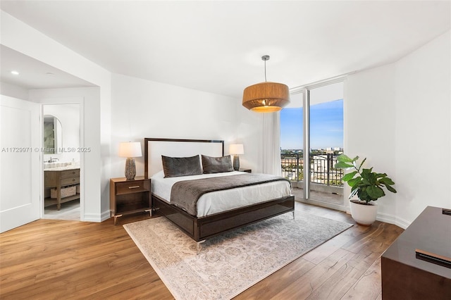 bedroom featuring arched walkways, baseboards, wood finished floors, access to outside, and expansive windows