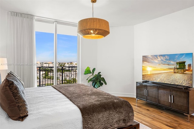bedroom featuring baseboards, a wall of windows, wood finished floors, and access to outside
