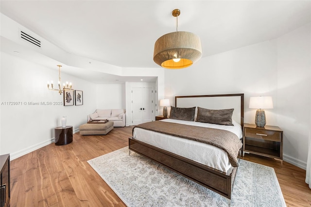 bedroom with an inviting chandelier, wood finished floors, visible vents, and baseboards