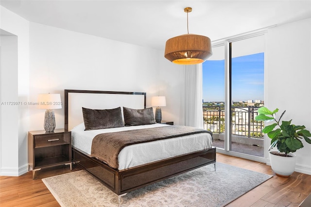 bedroom with expansive windows, wood finished floors, baseboards, and access to outside