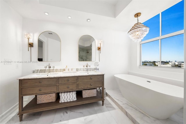 full bath featuring recessed lighting, marble finish floor, a freestanding bath, double vanity, and a notable chandelier