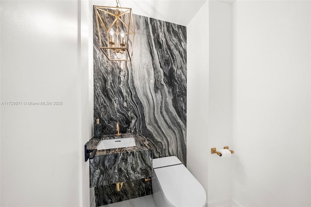 half bath featuring a chandelier, toilet, baseboards, and a sink