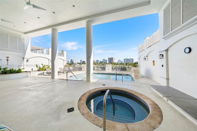 community pool featuring a city view, a hot tub, a patio area, and a ceiling fan