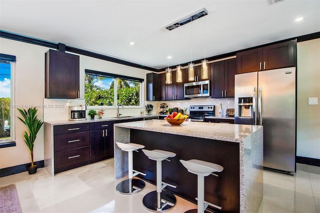 kitchen with a breakfast bar, backsplash, appliances with stainless steel finishes, a sink, and light stone countertops