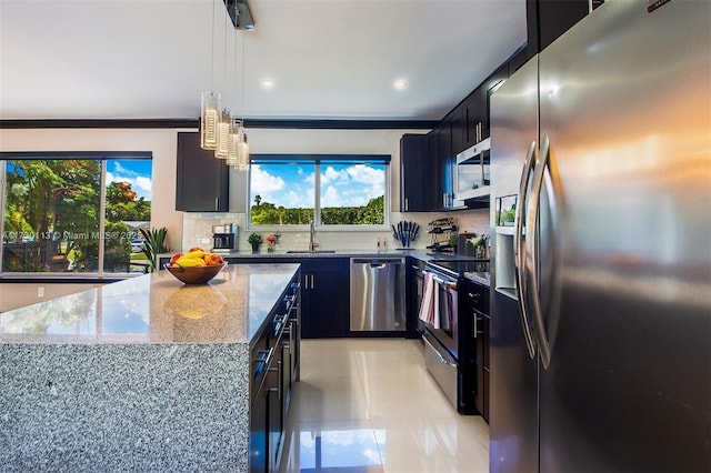 kitchen with tasteful backsplash, appliances with stainless steel finishes, a sink, light stone countertops, and dark cabinets