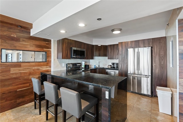 kitchen featuring sink, a breakfast bar area, appliances with stainless steel finishes, wooden walls, and kitchen peninsula