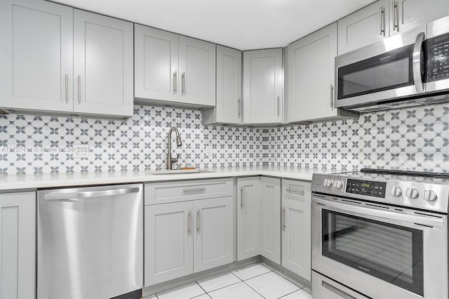 kitchen with appliances with stainless steel finishes, sink, gray cabinetry, decorative backsplash, and light tile patterned floors