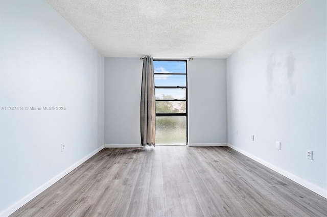 empty room featuring expansive windows, a textured ceiling, and light wood-type flooring