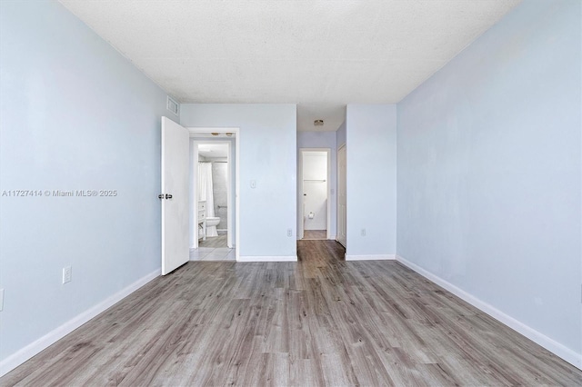 unfurnished bedroom featuring ensuite bathroom, a textured ceiling, and light hardwood / wood-style floors