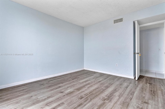 empty room with a textured ceiling and light hardwood / wood-style flooring