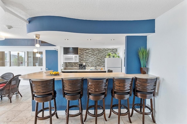 interior space with sink, backsplash, a kitchen breakfast bar, white appliances, and a textured ceiling