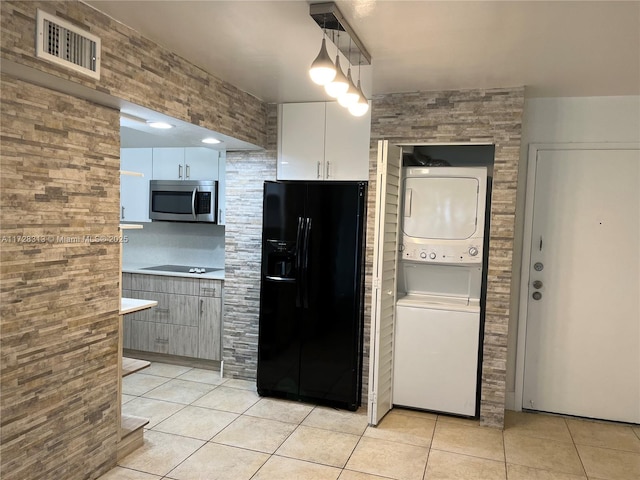 kitchen with hanging light fixtures, white cabinets, light tile patterned floors, stacked washer / dryer, and black appliances