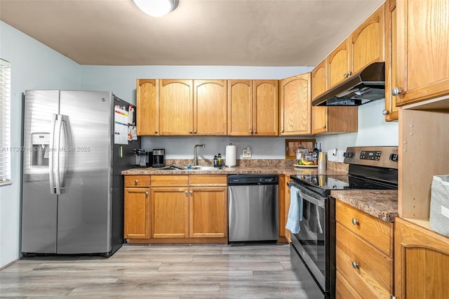 kitchen with sink, stainless steel appliances, dark stone countertops, and light hardwood / wood-style flooring