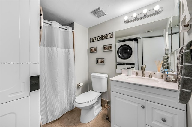 bathroom featuring toilet, vanity, stacked washer and dryer, and tile patterned flooring