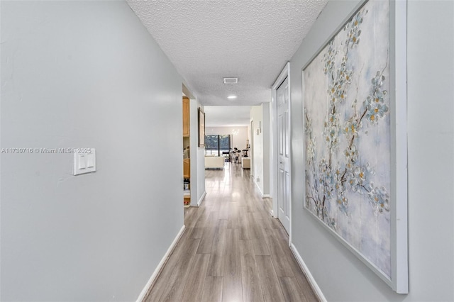 hall featuring a textured ceiling and light hardwood / wood-style flooring