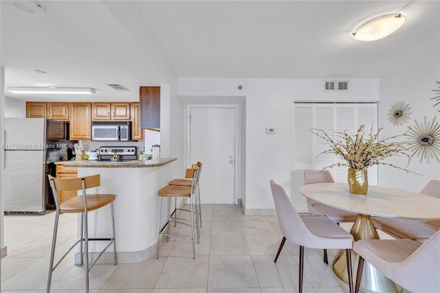 kitchen with appliances with stainless steel finishes, a breakfast bar area, light stone counters, and kitchen peninsula