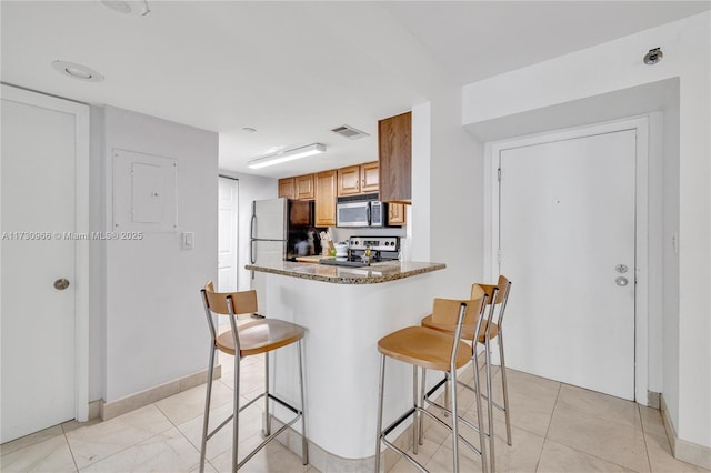 kitchen featuring stainless steel appliances, a kitchen breakfast bar, kitchen peninsula, and stone counters