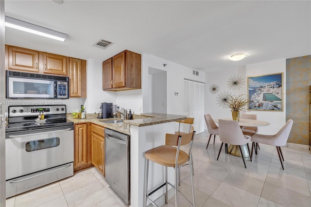 kitchen featuring a breakfast bar, sink, appliances with stainless steel finishes, kitchen peninsula, and light stone countertops