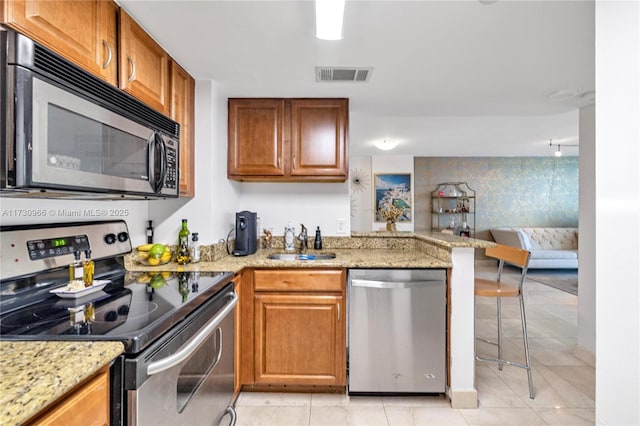 kitchen featuring appliances with stainless steel finishes, sink, light stone counters, and kitchen peninsula