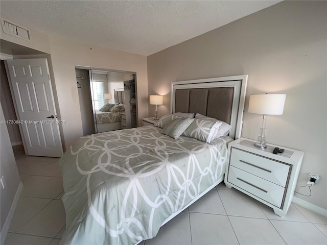 bedroom featuring visible vents, baseboards, light tile patterned floors, a closet, and a textured ceiling