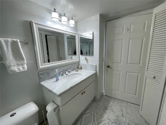 bathroom featuring vanity, toilet, marble finish floor, and a closet