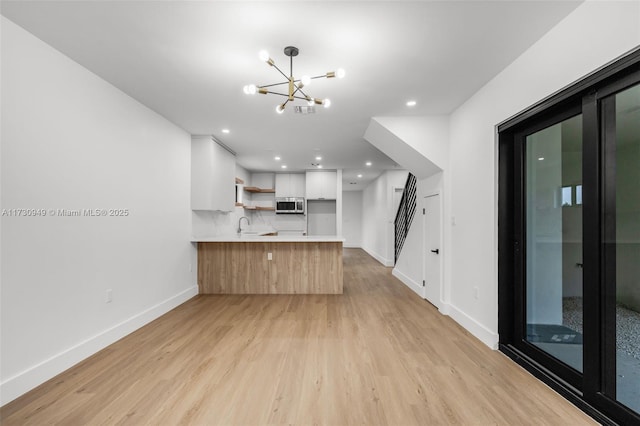 kitchen with sink, an inviting chandelier, white cabinets, kitchen peninsula, and light wood-type flooring