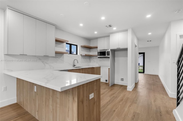 kitchen with backsplash, light stone countertops, kitchen peninsula, and white cabinets