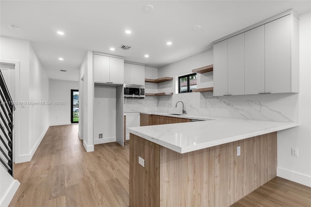 kitchen with sink, light wood-type flooring, kitchen peninsula, white cabinets, and backsplash