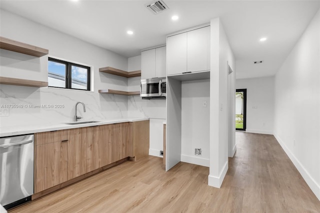 kitchen with sink, light hardwood / wood-style flooring, white cabinets, stainless steel appliances, and backsplash