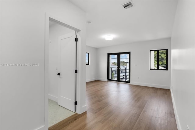 empty room with plenty of natural light, light hardwood / wood-style floors, and french doors