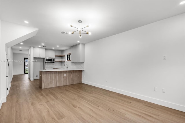 kitchen featuring sink, light hardwood / wood-style flooring, kitchen peninsula, a notable chandelier, and white cabinets